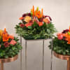 A trio of compact floral centerpieces arranged on copper-colored round trays creates