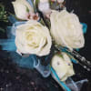 An elegant wrist corsage featuring classic white roses accented with decorative ribbon