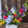 A fun birdhouse planter overflowing with colorful flowers including roses, hydrangea, snapdragons