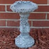 Decorative gray stone birdbath pedestal against a brick wall