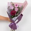 Handheld bouquet of pink roses and chrysanthemums wrapped in purple paper