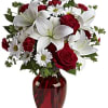 Bouquet of red roses, white lilies, and daisies in a red glass vase
