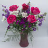 Vase arrangement with hot pink roses, purple flowers, and white blooms in a frosted pink glass vase