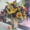 Bouquet of sunflowers, yellow roses, and magenta carnations in a glass vase