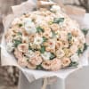 Large bouquet of blush roses, carnations, and white blooms wrapped in paper
