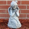 Gray praying angel statue in front of a brick wall