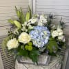 Mixed floral arrangement with white roses, blue hydrangea, and lilies in a silver container