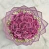 Round bouquet of purple roses with white filler flowers wrapped in lavender paper