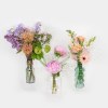 Three floral arrangements in glass vases with pink, purple, and peach blooms
