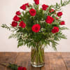 Red roses arranged in a clear glass vase with a matching rose on the table