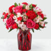 Pink roses, red carnations, and pale alstroemeria in a red glass vase