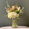Mixed bouquet with cream hydrangea, lilies, and pink accent flowers in a glass vase