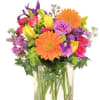Bright mixed bouquet of orange gerbera daisies, yellow tulips and purple blooms in a clear glass cube vase