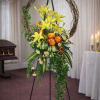 Standing floral spray with yellow lilies and orange roses on an easel