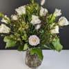 White roses arranged in a clear glass vase with greenery and small white accents