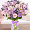 Pink and lavender bouquet of roses and daisies in a glass vase with a purple ribbon