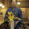 Man in a blue kimono holding a white vase of yellow and red flowers