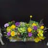 Bright yellow and purple floral arrangement in a low rectangular container