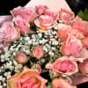 Hand-tied bouquet of pink roses with white filler flowers wrapped in soft pink paper