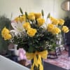 Yellow roses and white lilies in a clear glass vase with a yellow ribbon