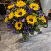 Bouquet of yellow sunflowers and purple filler flowers in a clear glass vase.