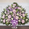 Large pastel floral arrangement with a purple ribbon on a pedestal vase