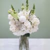 White floral arrangement in a clear glass vase with tall green spikes