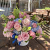Soft pink roses and ruffled carnations pair with clusters of blue hydrangea