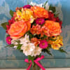 Mixed bouquet of orange roses, white lilies, and pink flowers in a glass vase