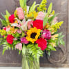 Mixed bouquet of roses, lilies, sunflowers, and carnations in a glass vase