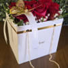 Red roses arranged in a white Dior gift box with a ribbon and gold butterfly decoration.