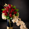 A dramatic cluster of velvety red roses crowns this floral arrangement, accented