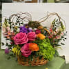 Basket arrangement with pink roses, orange ranunculus, and purple blooms