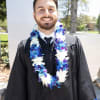 Man in graduation gown wearing a blue and white flower lei