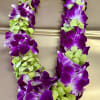 Purple and green orchid lei on a beige surface