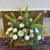 Large floral arrangement with pale roses, white blooms, and green spikes in a woven basket