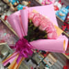 Pink rose bouquet wrapped in pink paper with a purple ribbon