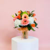 A bright peach gerbera takes center stage in this rounded flower arrangement