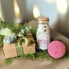 Gift box with ribbon, bath salt jar, and pink bath bomb on greenery