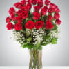 Tall arrangement of red roses with white filler flowers in a clear glass vase