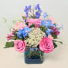 Pink roses and blue flowers arranged in a square glass vase