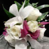 White roses and calla lilies arranged in a glass vase with magenta ribbon accents.