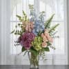 Mixed bouquet of roses, hydrangeas, and blue delphinium in a glass vase