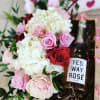 Pink and red roses with white hydrangeas beside a bottle of rosé