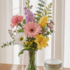 Mixed bouquet in a clear glass vase with pink, yellow, white, and purple flowers