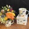 Orange and yellow flower arrangement in a dragonfly mug beside a matching mug and box