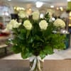 White roses arranged in a clear glass vase with a white ribbon