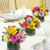Three small floral centerpieces in square glass vases on a table