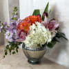 Round, lush mix of white hydrangea, orange roses, pink orchids, tulips and