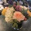 Low glass vase of peach roses, white hydrangeas, and mixed pastel flowers on a green countertop.